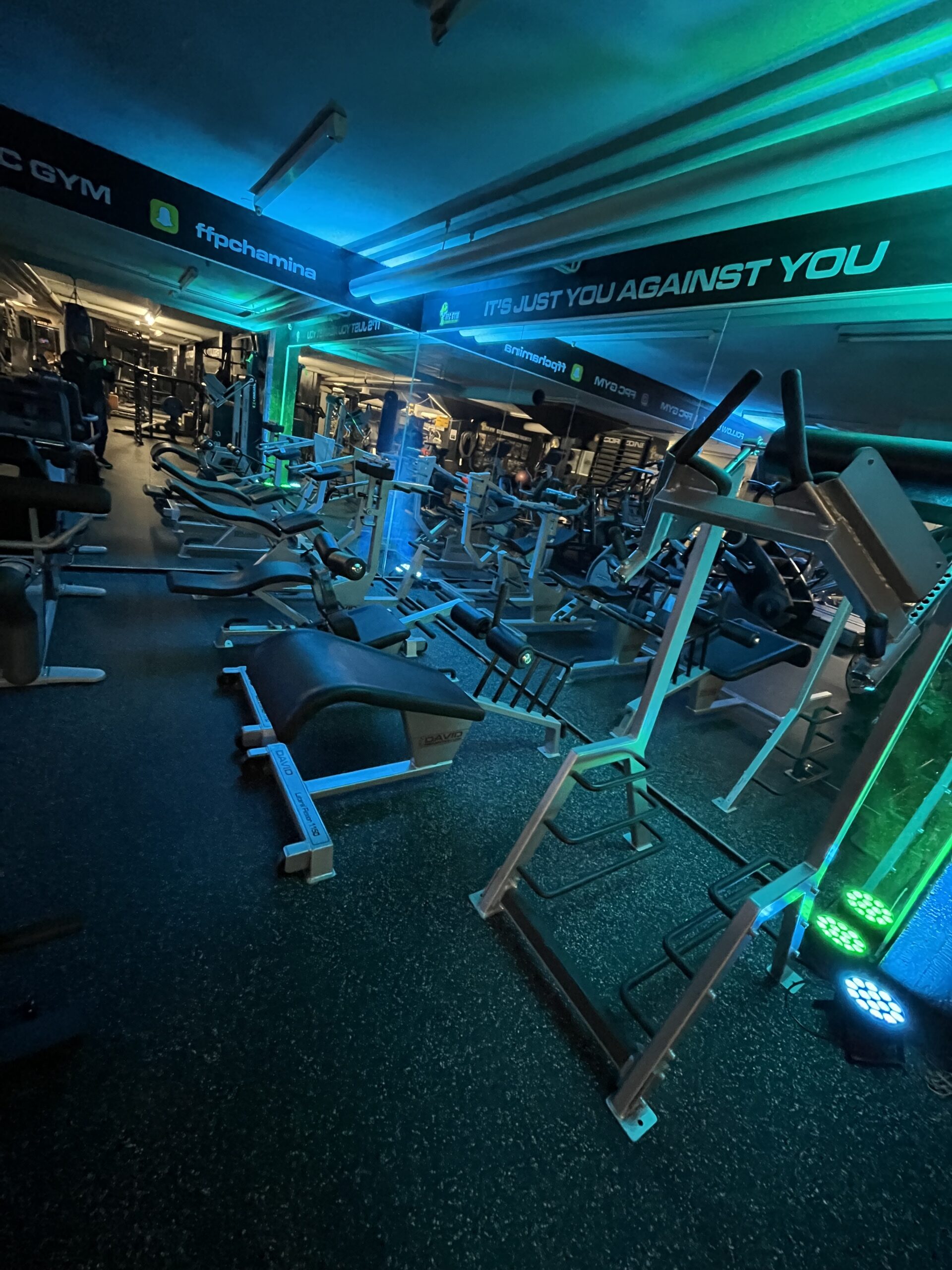 Kuvassa on FPC GYM - Hamina kuntosalin sali, jossa on monipuolinen valikoima kuntolaitteita, painonnostotekstiilejä ja treenivälineitä, valaistus luo energisen ja inspiroivan treenikokemuksen.
